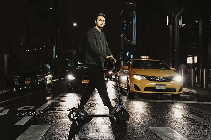 Hombre conduciendo de noche un patinete eléctrico Micro Merlin X4 - Normativa de los patinetes eléctricos en 2023